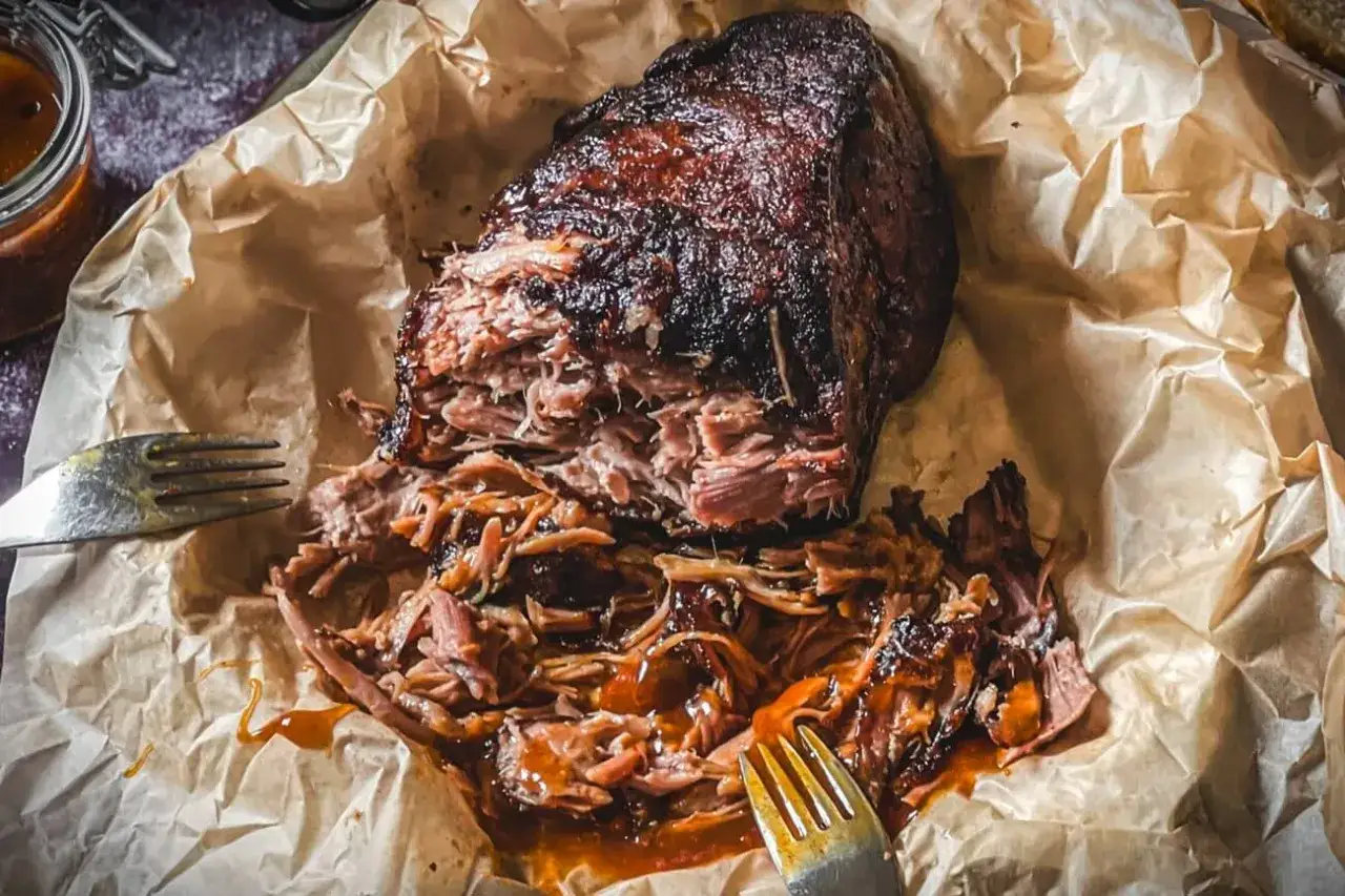 Saftiges Pulled Pork, perfekt zubereitet mit einem k&ouml;stlichen pulled pork rub, liegt auf Backpapier. Zwei Gabeln warten darauf, das zarte Fleisch zu zerteilen.
