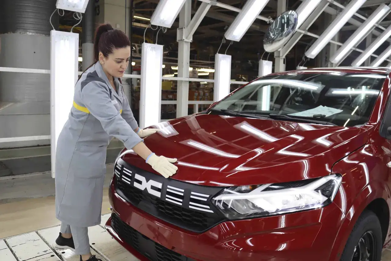 Pracownica w fabryce sprawdza błyszczącą maskę czerwonego Dacia, samochodu, którego kraj pochodzenia to Rumunia.