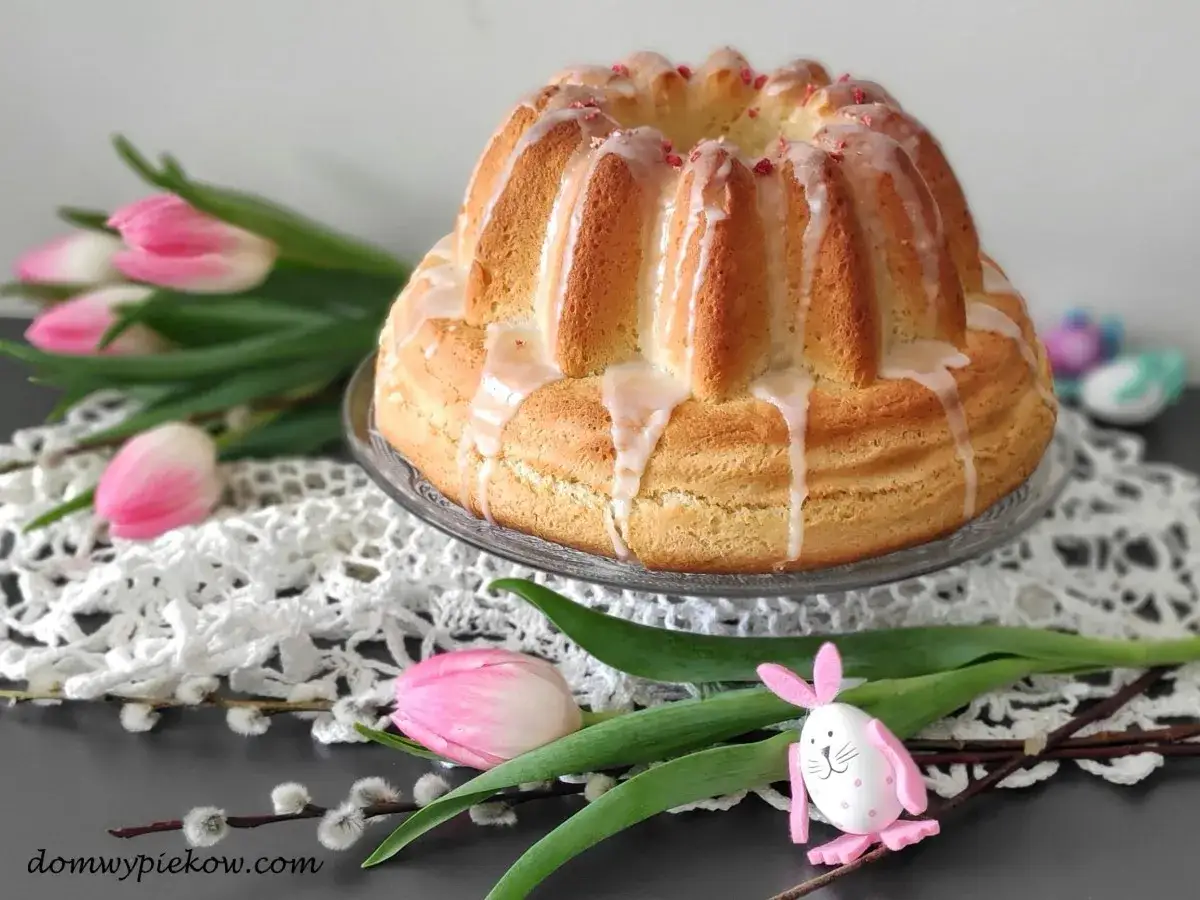 Babka drożdżowa przepis babci, udekorowana lukrem i posypką, otoczona wiosennymi tulipanami i baziami.