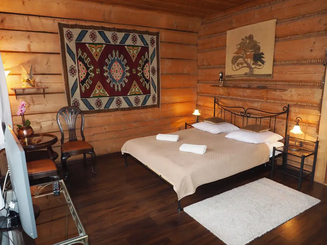 Przytulny pok&oacute;j w stylu g&oacute;ralskim, idealny hotel dla kot&oacute;w. Drewniane ściany, ł&oacute;żko, dywaniki i ozdobne tkaniny tworzą ciepłą atmosferę.