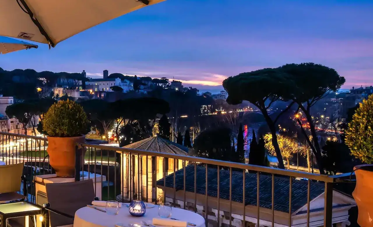 Romantisches Abendessen mit Blick auf die Stadt bei D&auml;mmerung. Ein Tisch ist gedeckt, Lichter glitzern in der Ferne. Ein echter Geheimtipp f&uuml;r Rom.