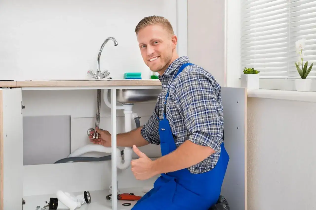Plumber working under a sink, showing how to replace kitchen faucet. He gives a thumbs up.