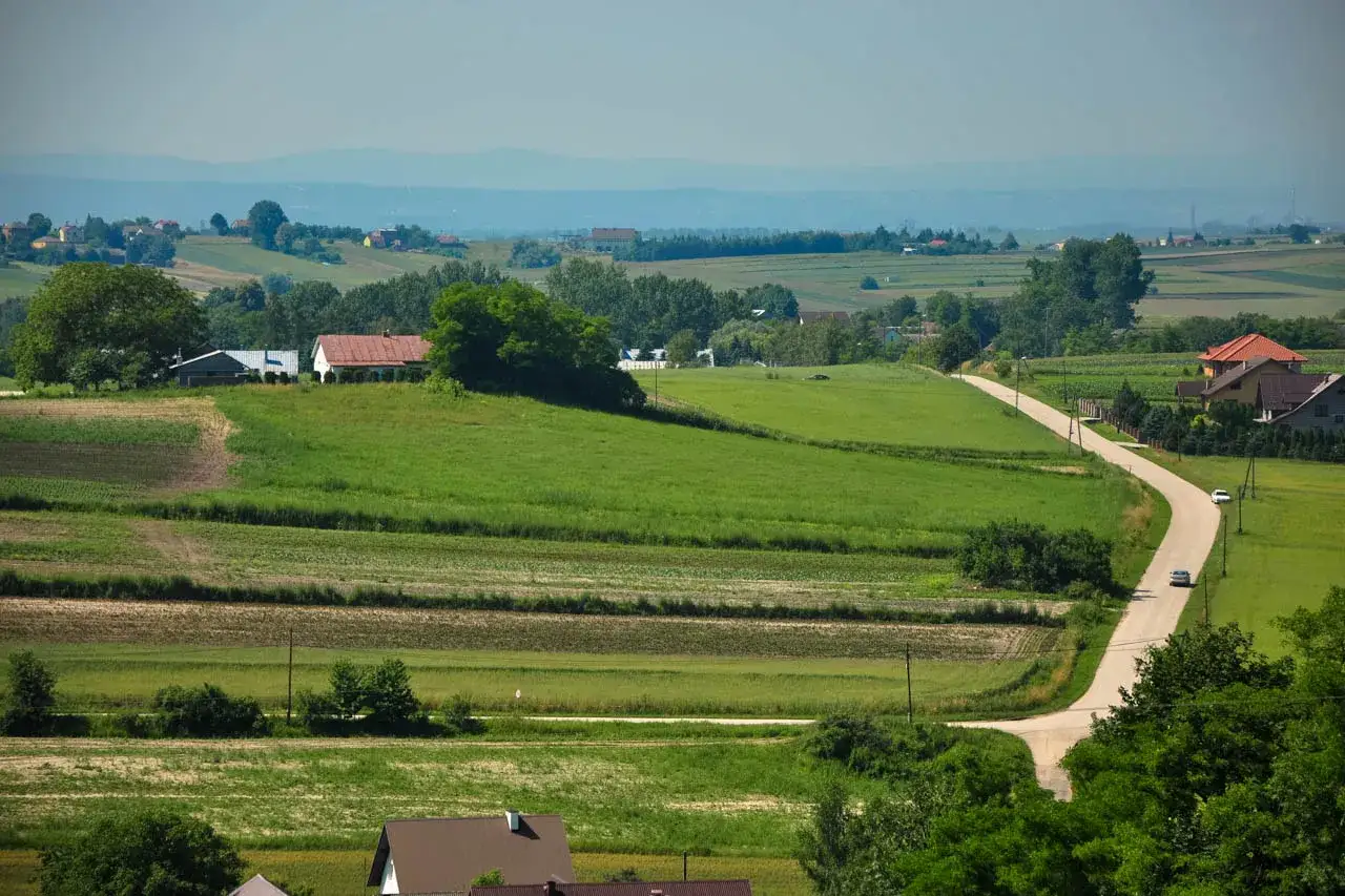 Krajobraz wiejski z drogą, domami i polami. Rozważasz sprzedaż działki z warunkami zabudowy, a VAT?