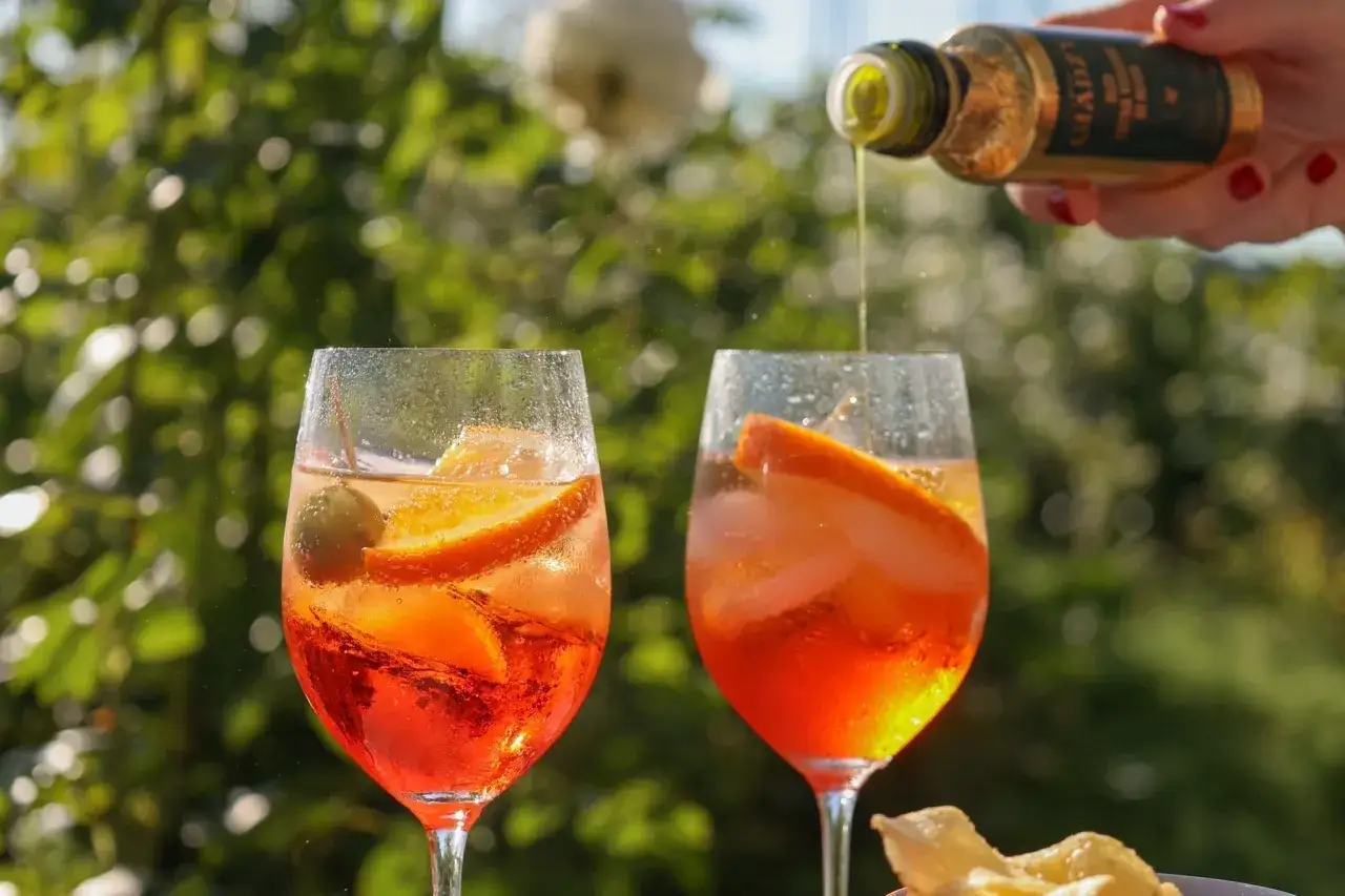 Zwei Gläser Veneto Spritz mit Orangen und Oliven, während ein Schuss aus einer Flasche hinzugefügt wird.