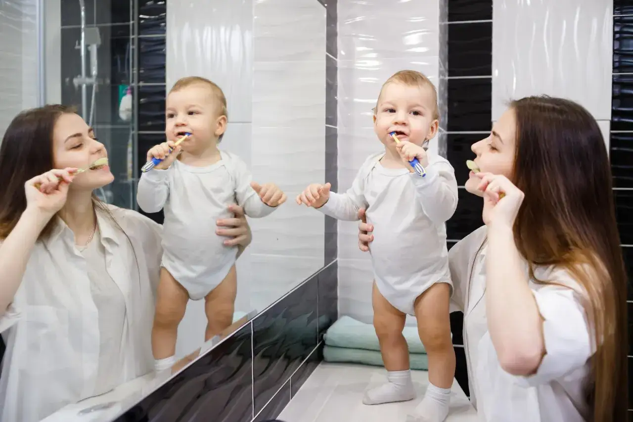 Mama uczy maluszka, jak myć zęby niemowlakowi. Uśmiechnięty chłopczyk z mamą szczotkują ząbki przed lustrem.