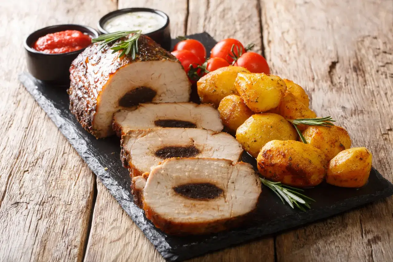 Pyszny schab ze śliwką, pieczone ziemniaczki, pomidorki i sosy. Idealny obiad na drewnianym stole.