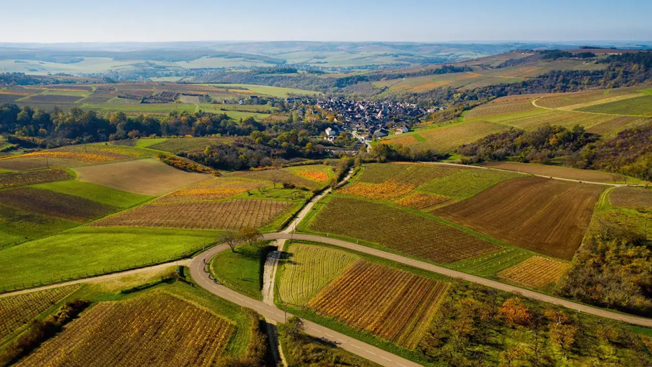 Vue a&eacute;rienne d'un village pittoresque en **Bourgogne**, entour&eacute; de vignobles aux couleurs d'automne et de champs verdoyants.