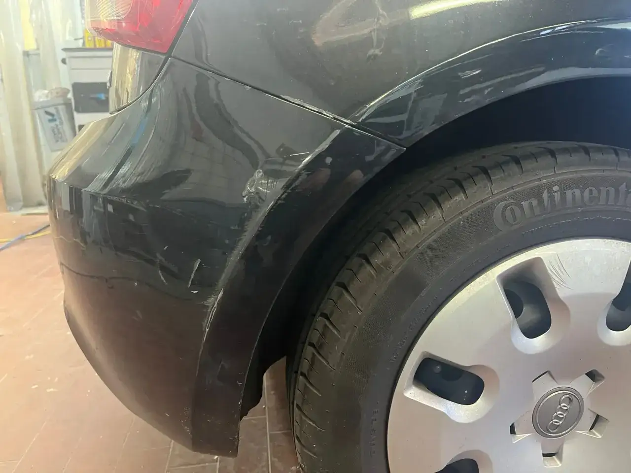 En svart bil med en djup repa i lacken på bakskärmen, precis ovanför däcket.