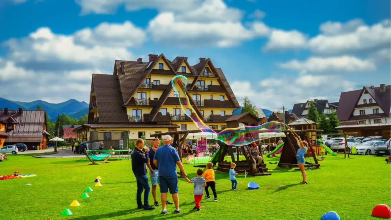 Zakopane atrakcje dla dzieci latem: rodzina obserwuje gigantyczne bańki mydlane na zielonym trawniku przed hotelem.