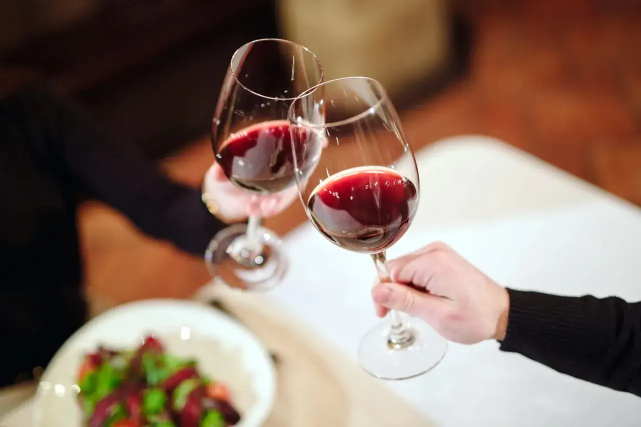 Zwei Gläser mit tiefrotem **Wein rot** stoßen an. Im Vordergrund ein Salat.
