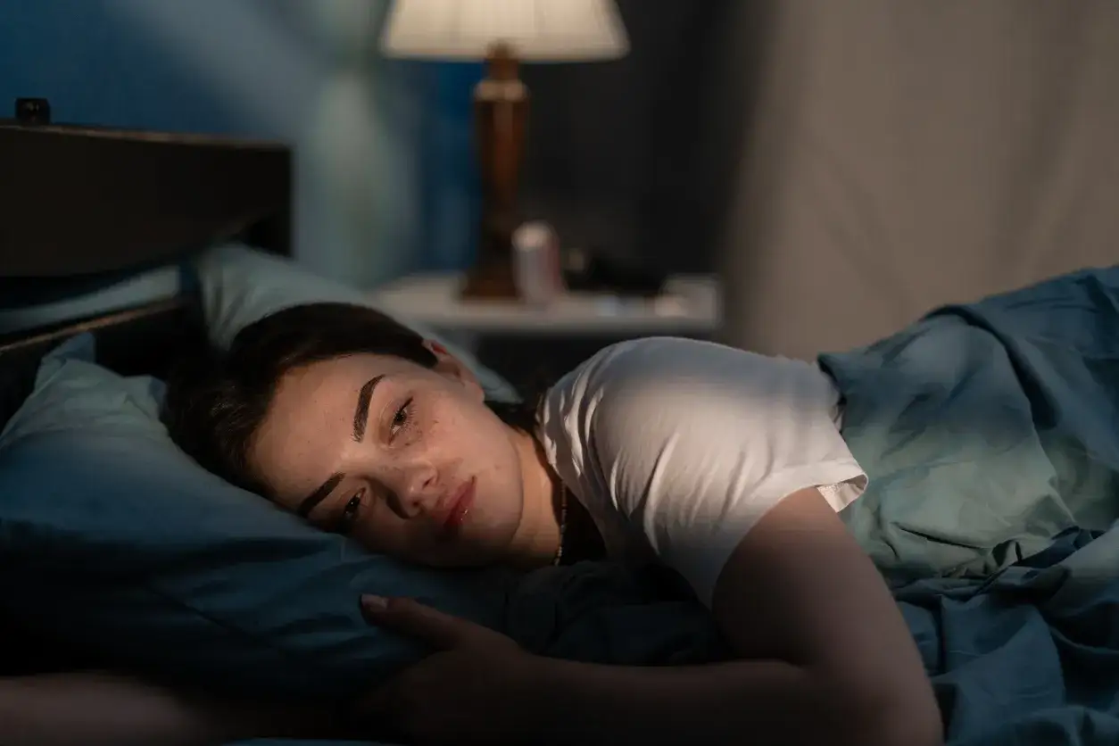 A young woman lies in bed, looking tired and thoughtful. Is four hours of sleep enough for her to feel rested?