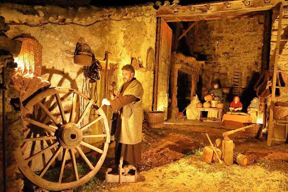 Belén viviente en Buitrago de Lozoya en Navidad. Un hombre trabaja una rueda de molino mientras figuras femeninas preparan vasijas.