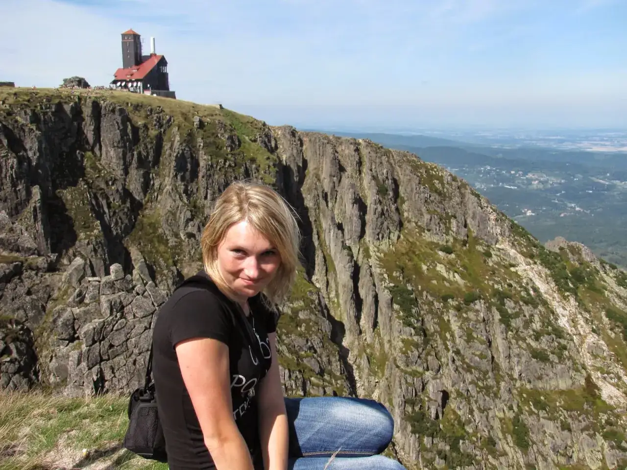 Kobieta na tle górskiego krajobrazu z budynkiem na szczycie. Wielki szyszak szlak zaprasza do podziwiania widoków.