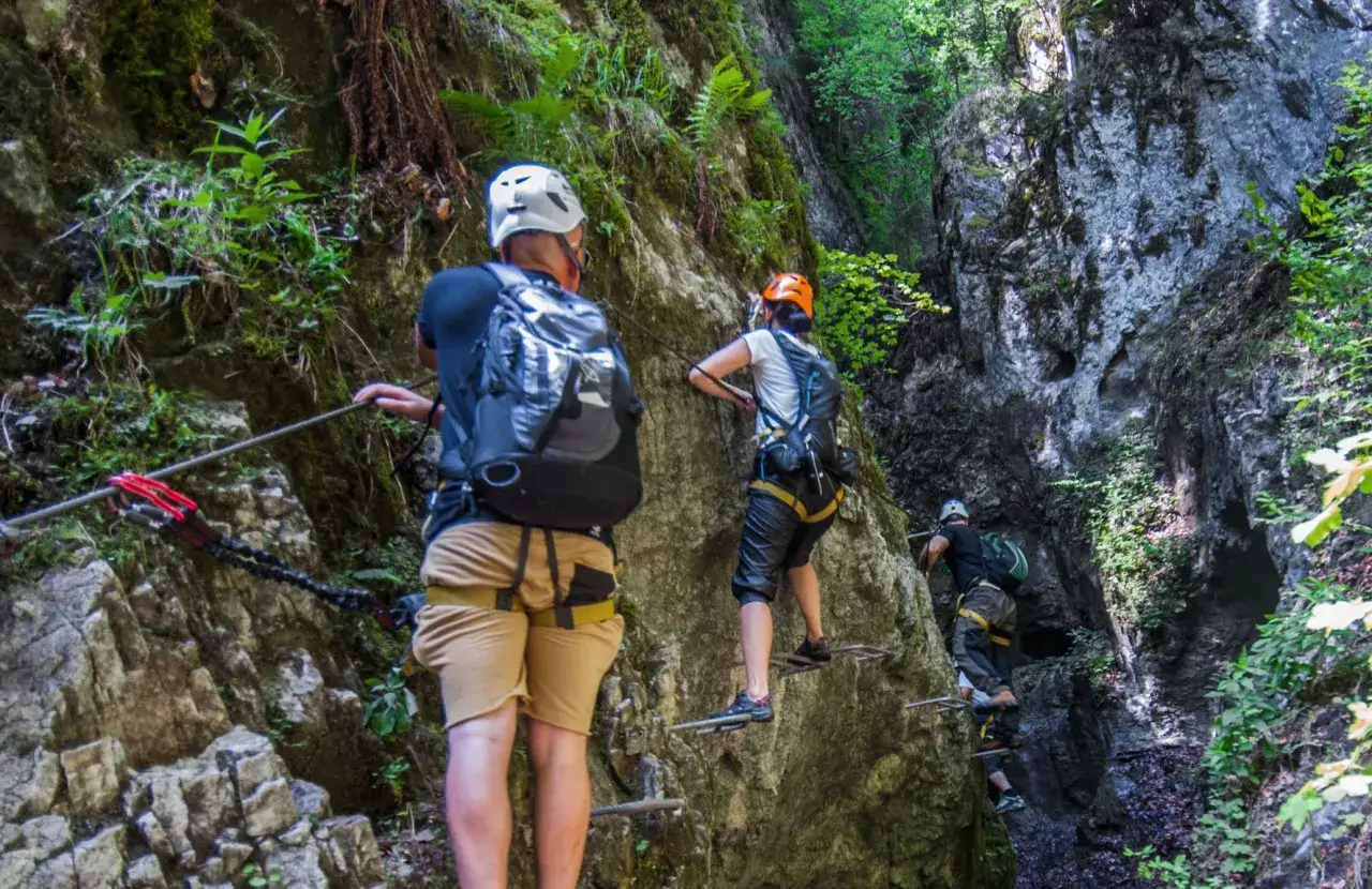 Trzej turyści pokonują trudną trasę słowacki raj via ferrata, wspinając się po skalnej ścianie z pomocą stalowych lin i drabinek.