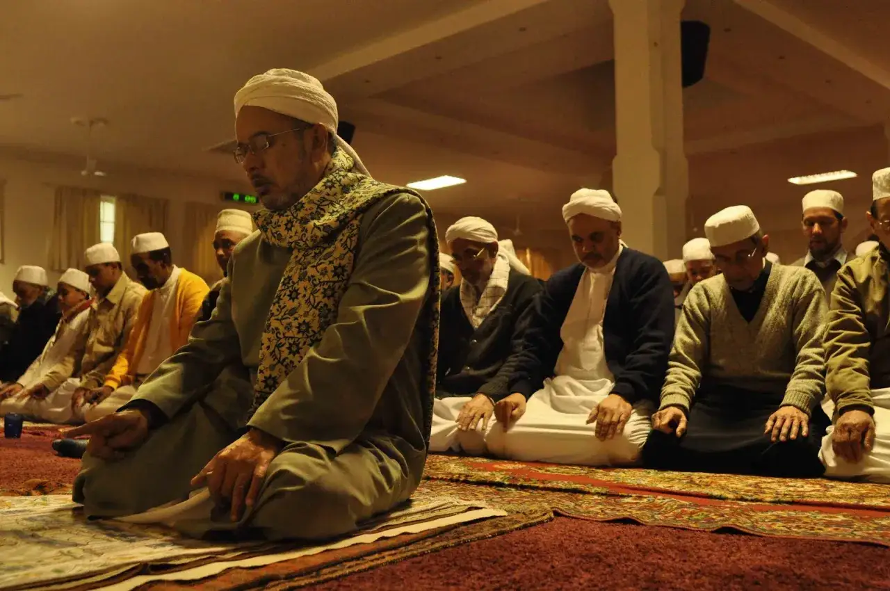 Männer in weißen Turbanten und traditioneller Kleidung knien auf Gebetsteppichen und verrichten das Taraweeh-Gebet.