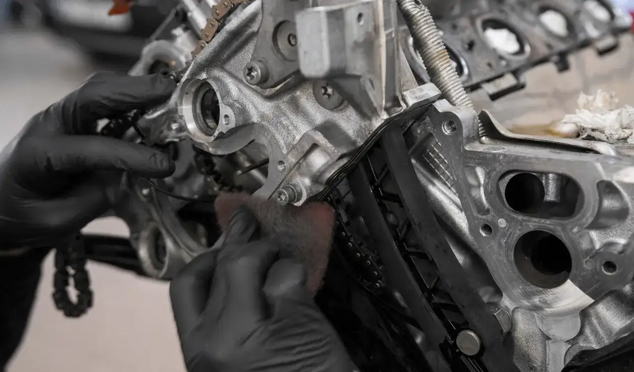 Mechanik w czarnych rękawiczkach czyści silnik, przygotowując go do wymiany łańcucha rozrządu.