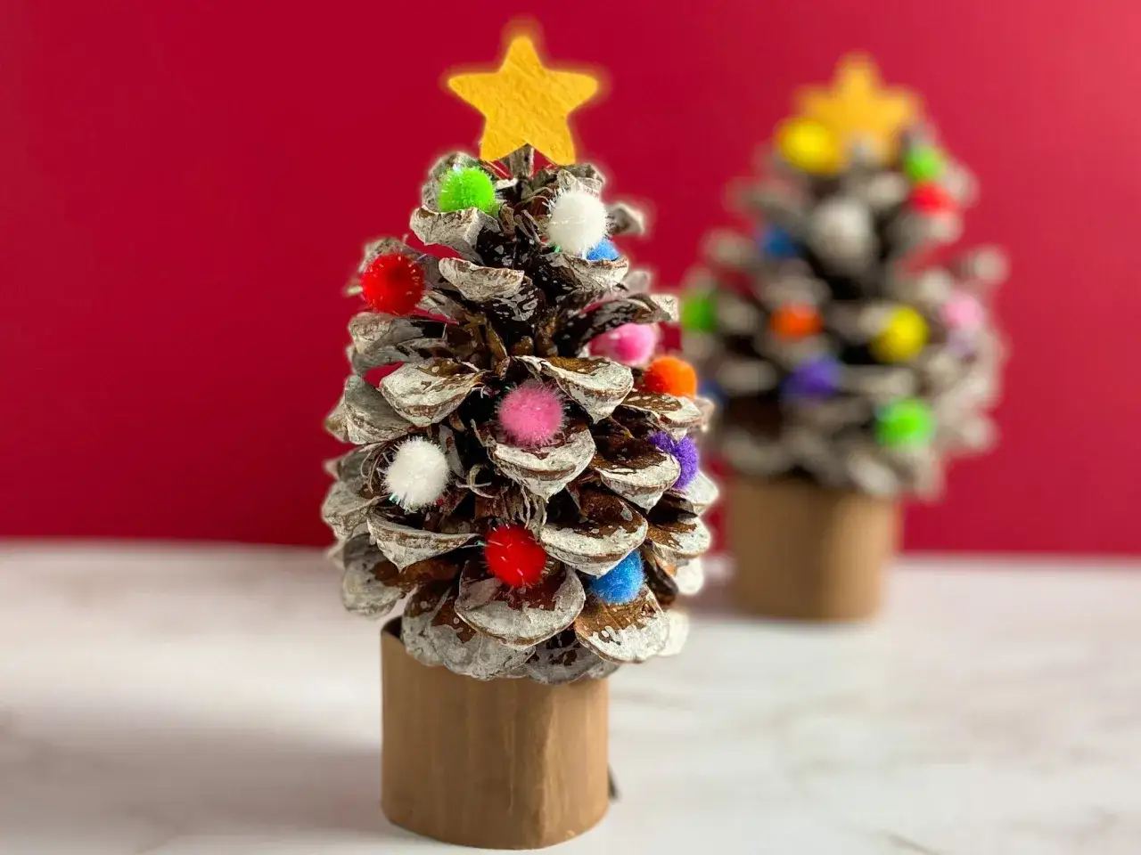 Julgranar gjorda av kottar, dekorerade med f&auml;rgglada pom-poms och en gul stj&auml;rna. Ett roligt pyssel med kottar f&ouml;r julen!
