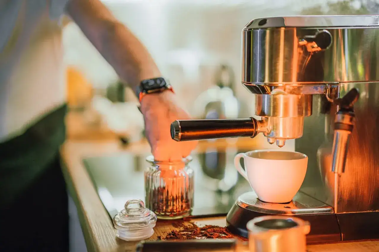 Ręka wsypuje ziarna kawy do ekspresu, by zrobić idealne espresso.