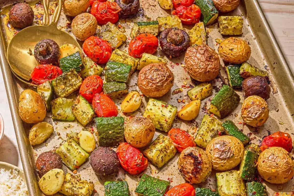 Plaque de légumes grillés au four : pommes de terre, courgettes, tomates cerises et champignons, assaisonnés d'herbes et d'épices.