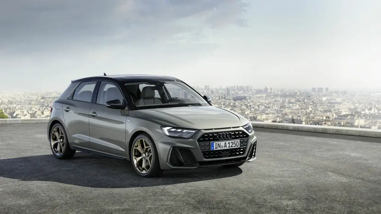 Szary Audi RS1 z brązowymi felgami stoi na dachu z widokiem na miasto.