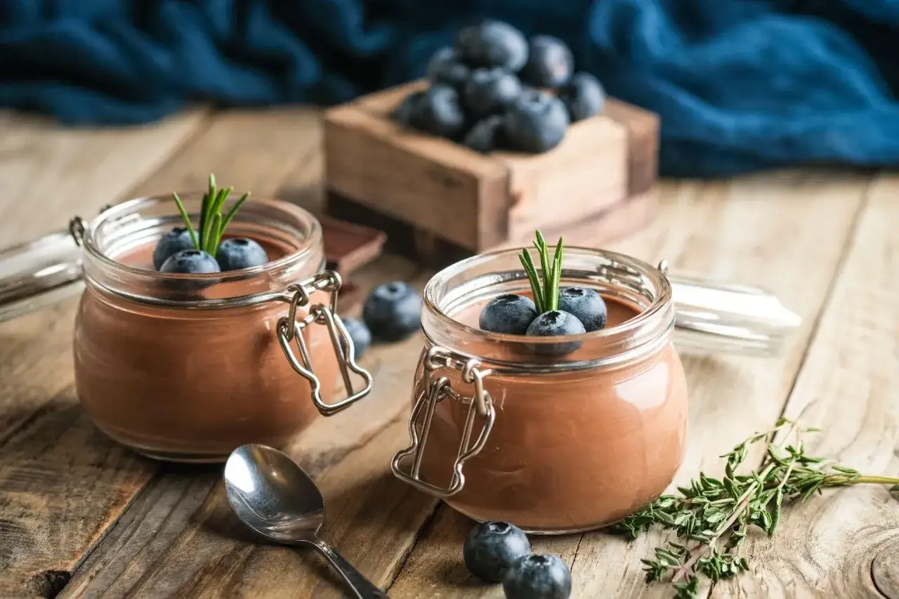 Dwa słoiczki pysznego, czekoladowego mousse po polsku, udekorowane borówkami i gałązką rozmarynu.