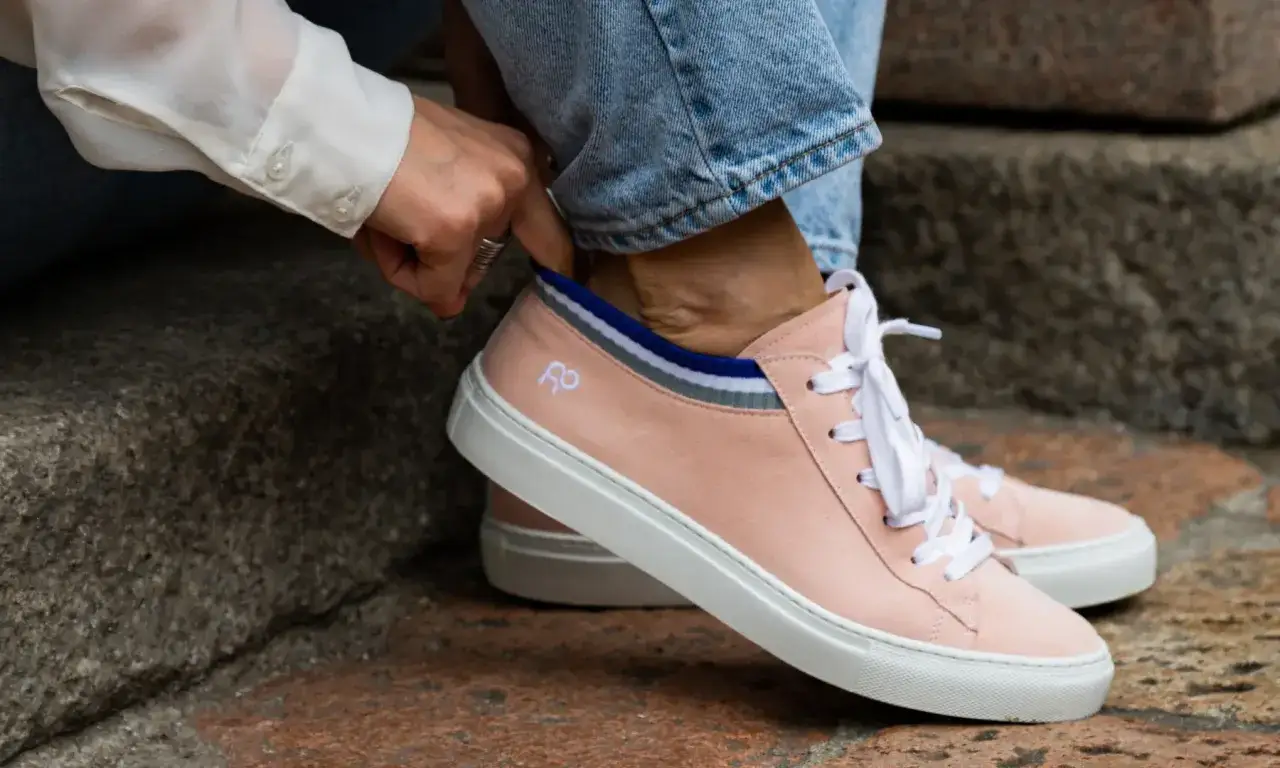 Mani che sistemano calzini a righe dentro scarpe rosa cipria, un dettaglio di riempimento scarpe grandi per un look casual.