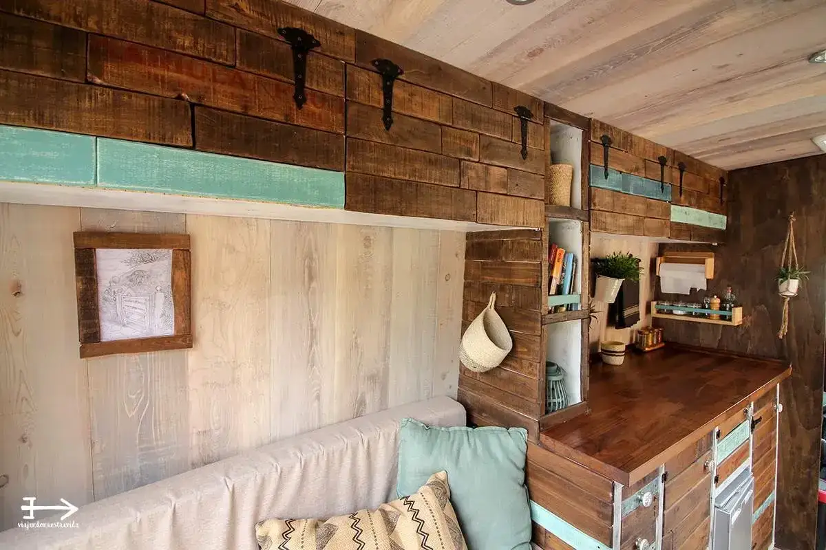 Interior de una caravana camperizada con muebles de madera rústica, sofá y estanterías.