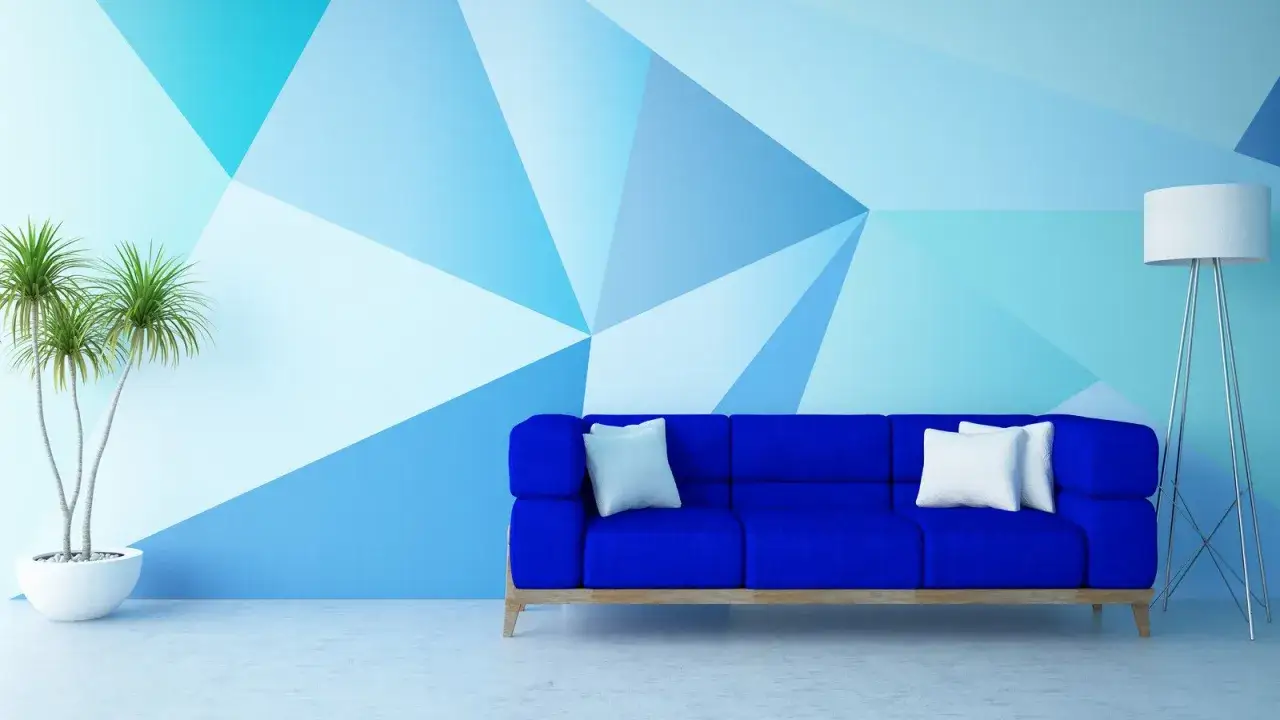 Niebieska sofa i roślina stoją przed ścianą z geometrycznymi wzorami w odcieniach błękitu.