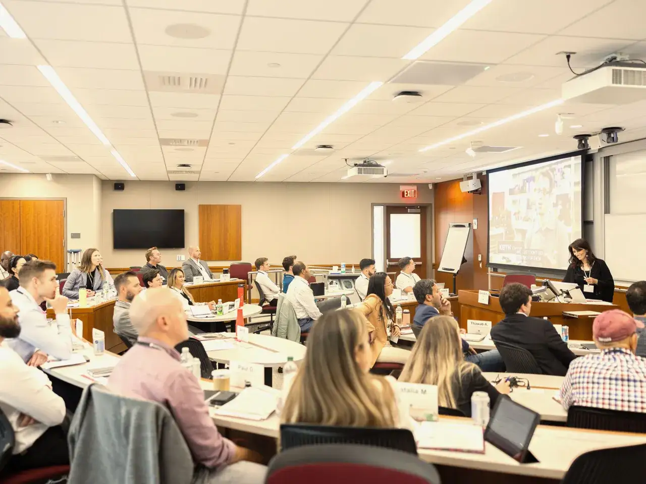 Attendees at negotiation seminars listen intently to a speaker presenting on a large screen.