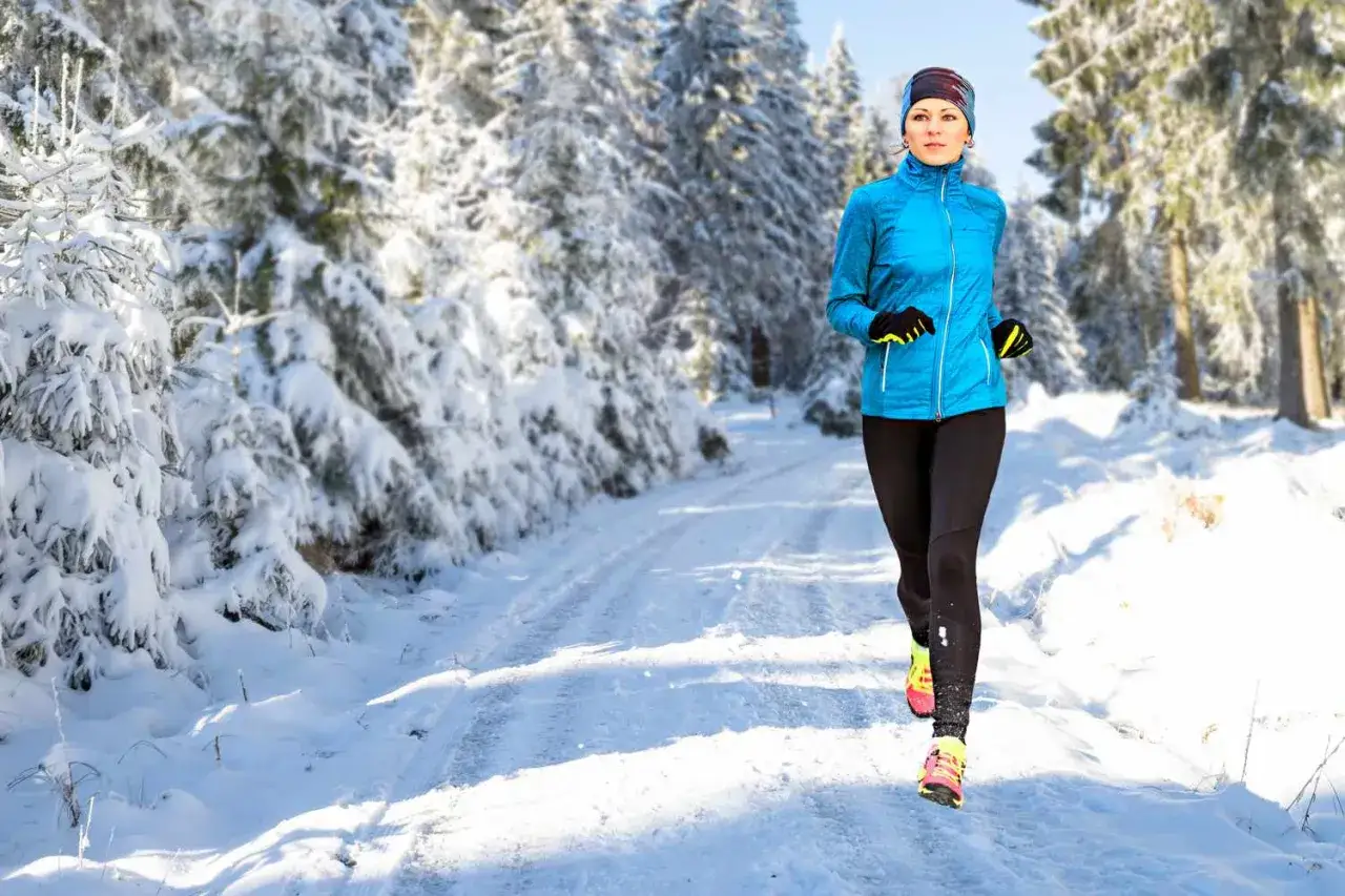 Donna corre su sentiero innevato tra alberi coperti di neve, nonostante la tosse, determinata a mantenere la sua routine di allenamento invernale.