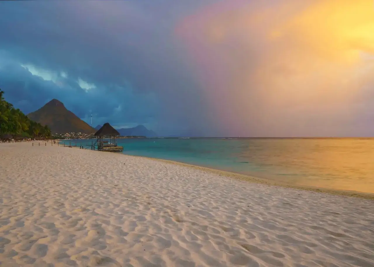 Plaża na Mauritiusie w lutym. Piasek, turkusowa woda, góry w oddali i chmury malujące niebo.