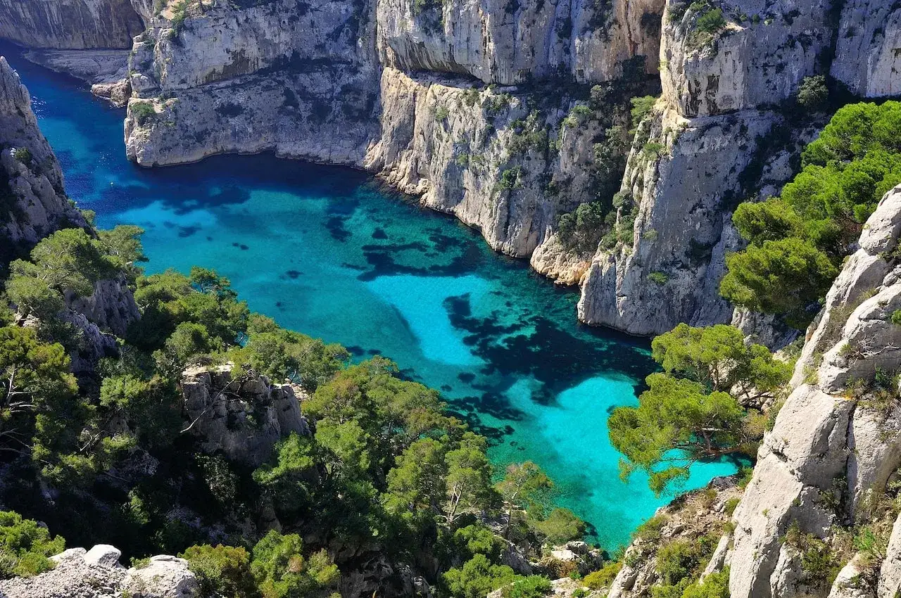 Vue a&eacute;rienne d'une calanque aux eaux turquoise, un endroit paradisiaque en France, entour&eacute;e de falaises calcaires et de pins verts.
