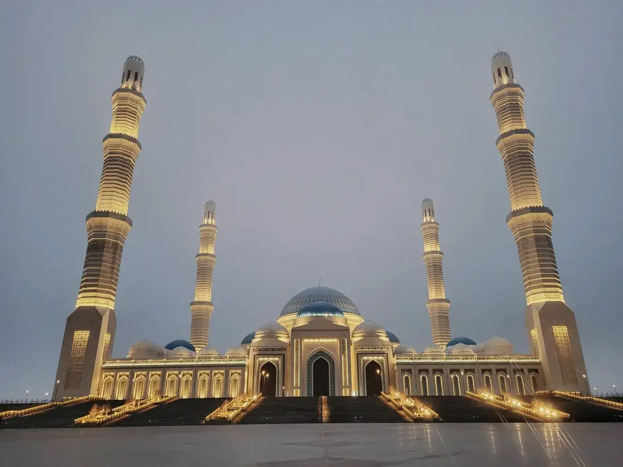 Die imposante Astana Moschee erstrahlt im Abendlicht, ihre Minarette und Kuppeln sind beleuchtet.
