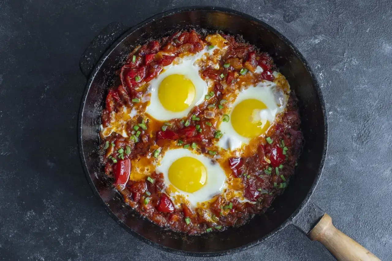 &OElig;ufs poch&eacute;s dans une sauce tomate &eacute;pic&eacute;e, une d&eacute;licieuse recette de chakchouka, garnie de ciboule fra&icirc;che.