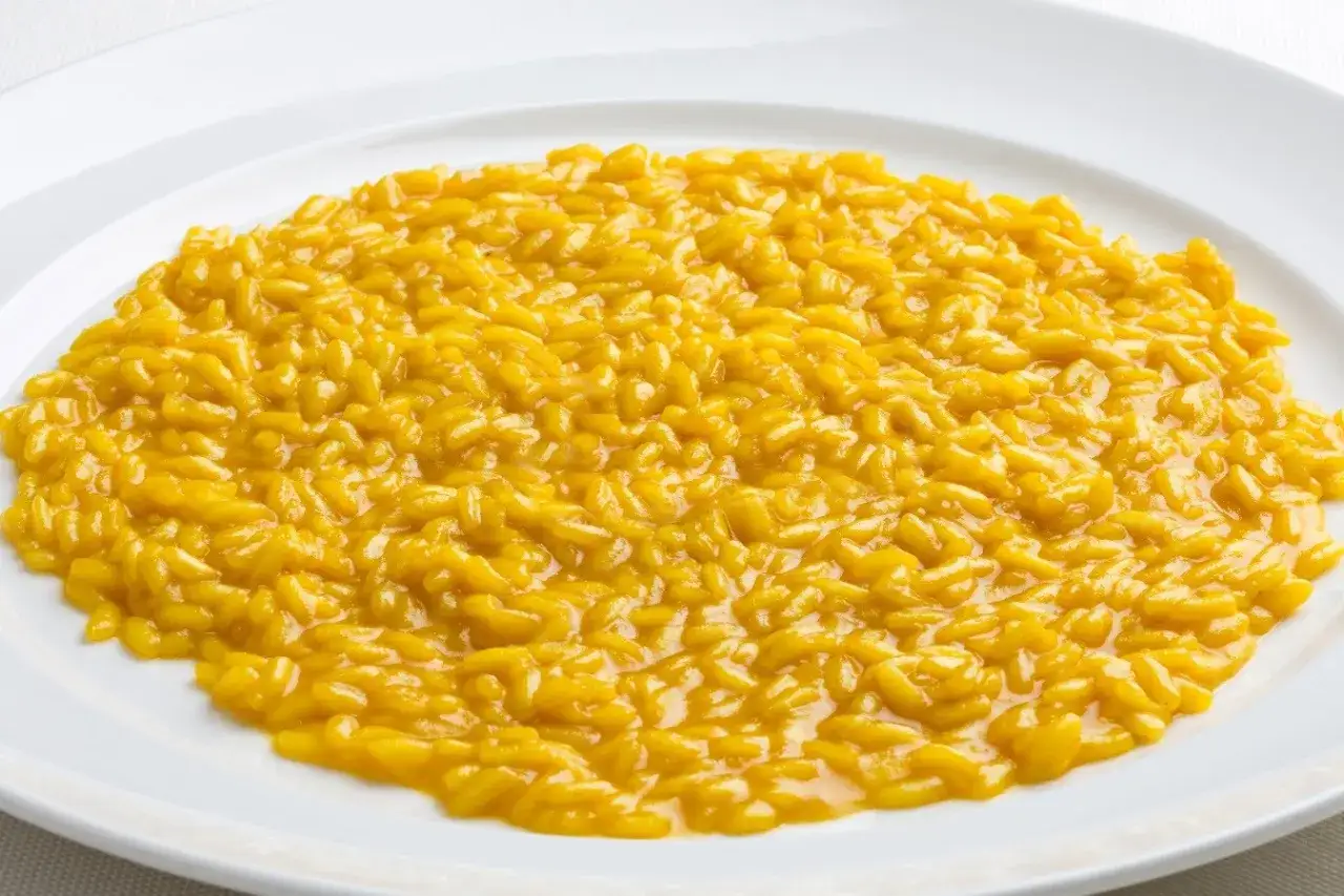 Un cremoso risotto allo zafferano, dal colore dorato intenso, servito su un piatto bianco.
