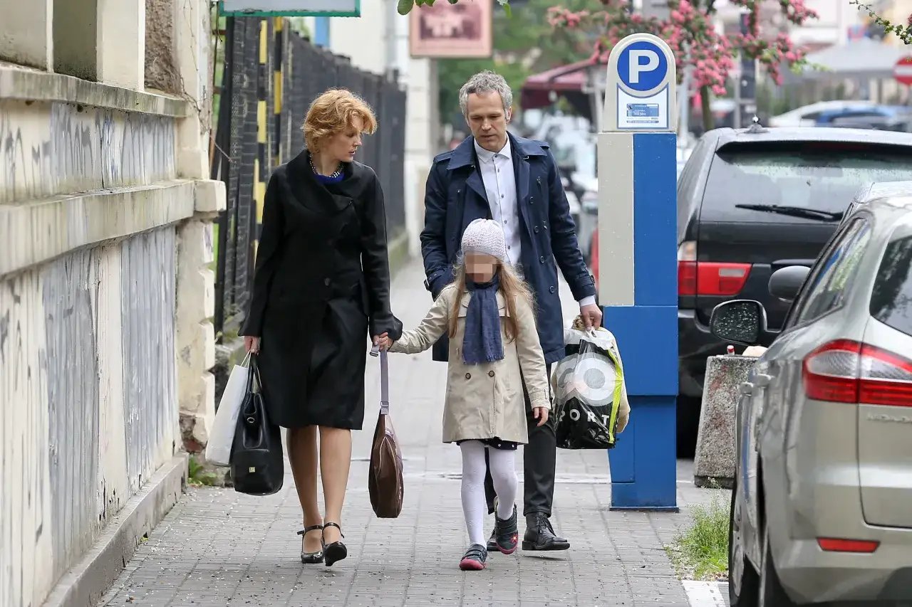 Klara Maria Pazura z rodziną spaceruje po chodniku, trzymając się za ręce.