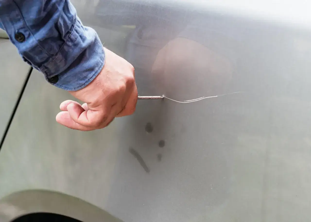 Mano con cacciavite graffia la portiera di un'auto, un atto vandalico che lascia segni indelebili.