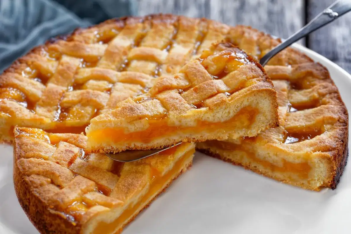 Deliziosa crostata senza glutine con ripieno di albicocche, la fetta sollevata mostra la morbidezza e il colore invitante.