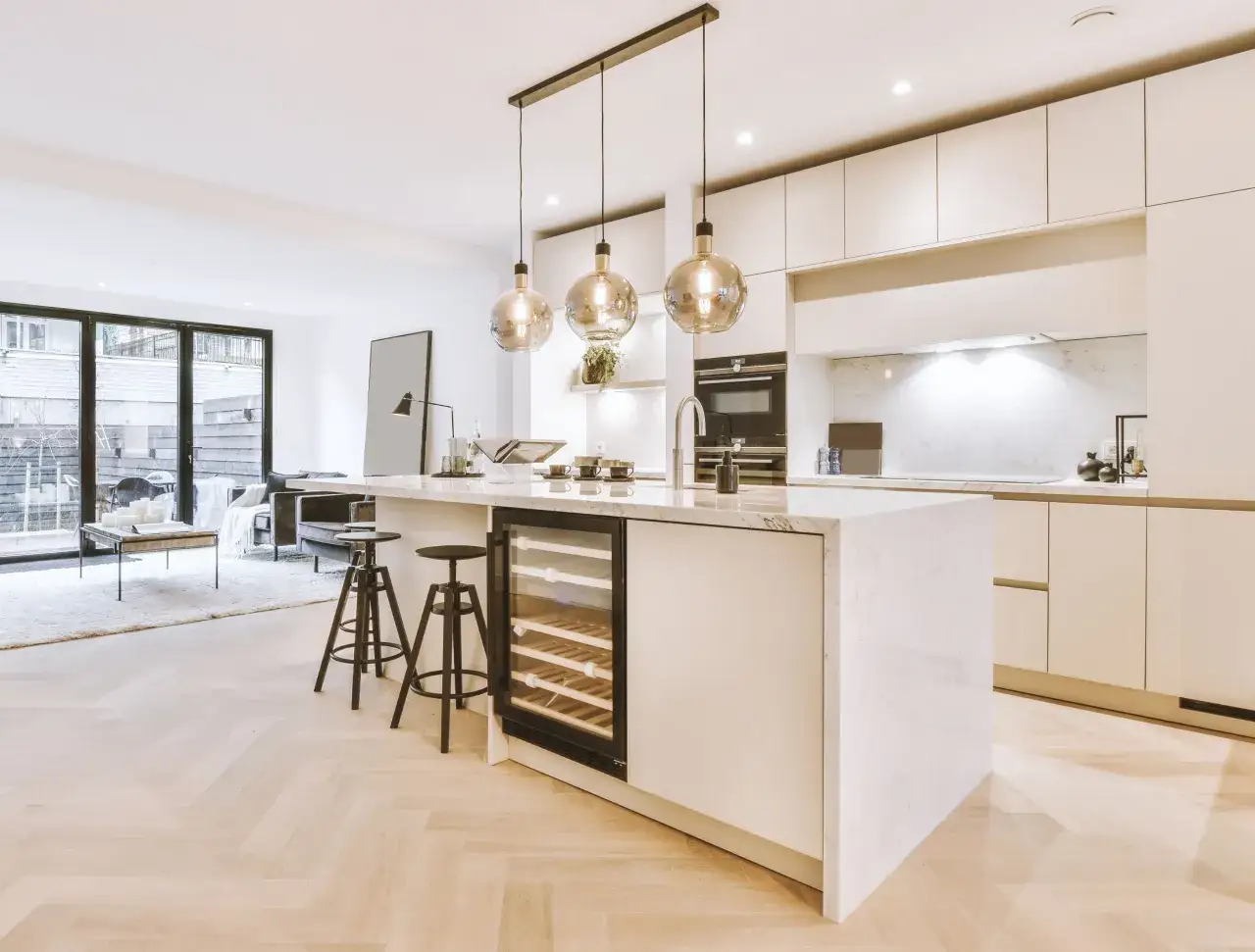 Moderna cocina con isla central, vinoteca y tres l&aacute;mparas colgantes sobre ella.