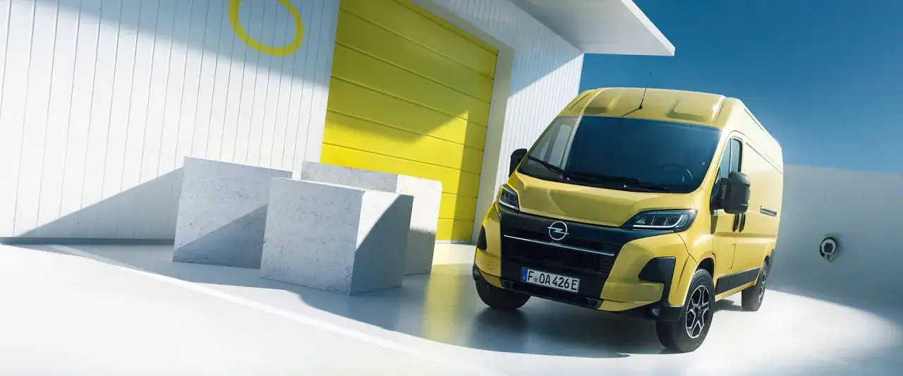 En gul Opel Movano st&aring;r parkerad framf&ouml;r en vit byggnad med en gul port. Betongblock ligger utspridda p&aring; marken.