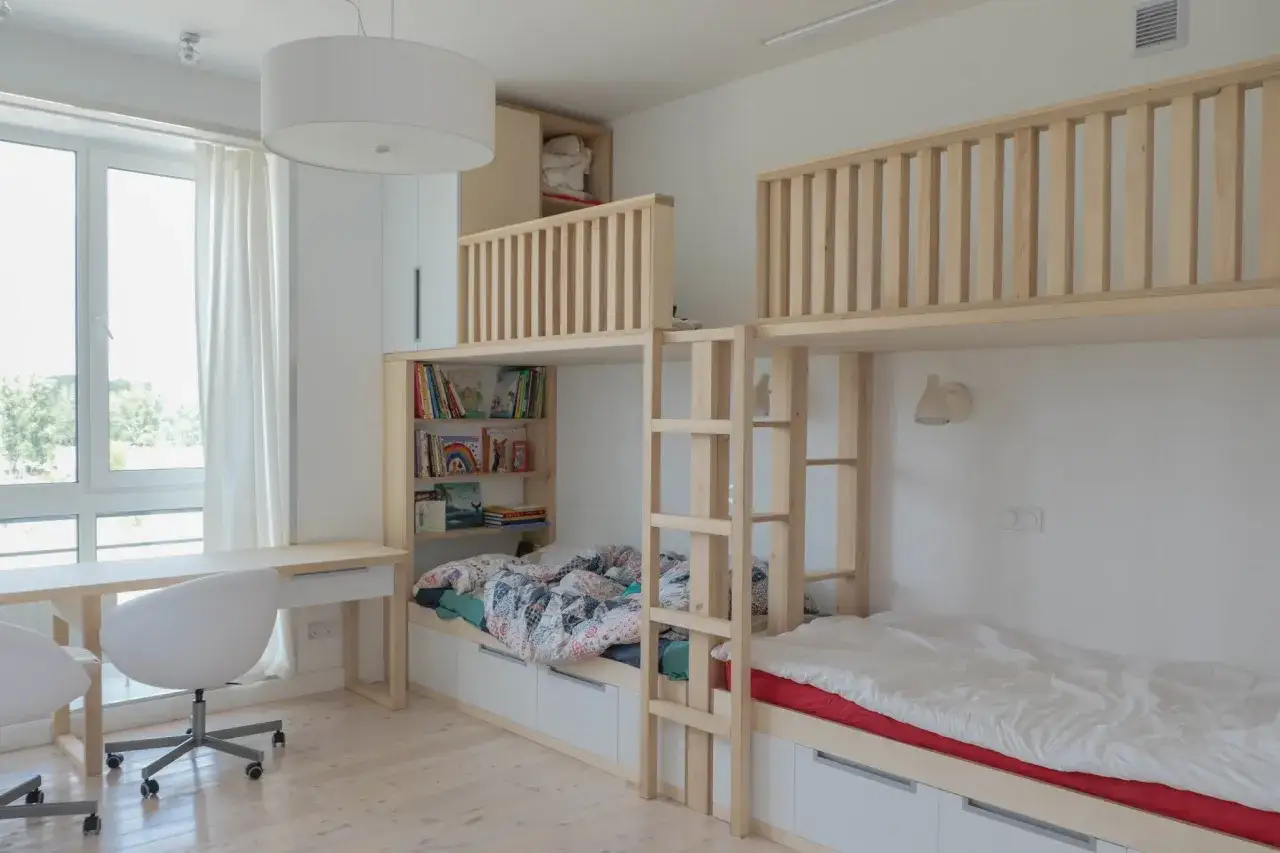 Ljust och modernt barnrum med två sängar i en våningssängslösning i trä. Bokhyllor och förvaring integrerat.