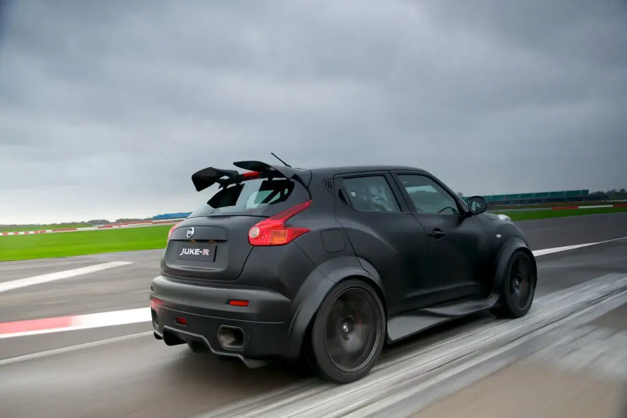 Czarny Nissan Juke-R z potężnym spojlerem pędzi po torze wyścigowym.