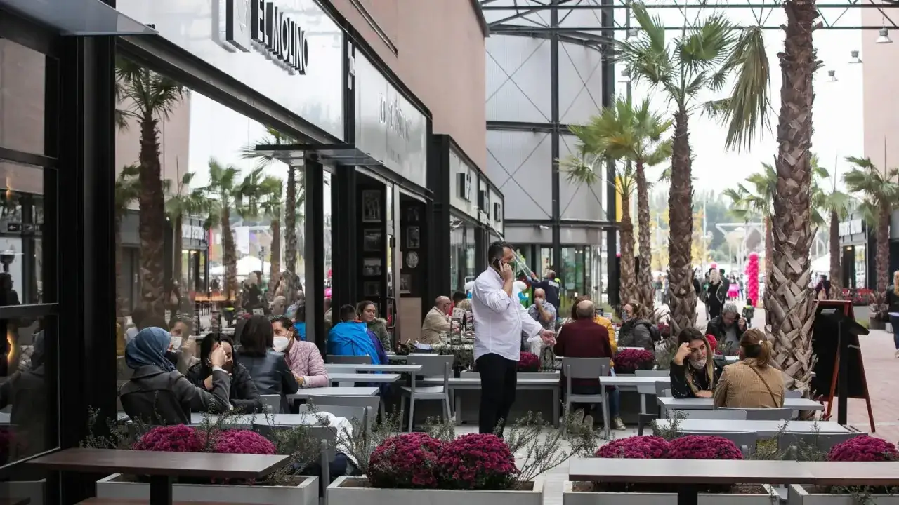 Gente disfrutando en los restaurantes de la torre outlet, rodeados de palmeras y flores.