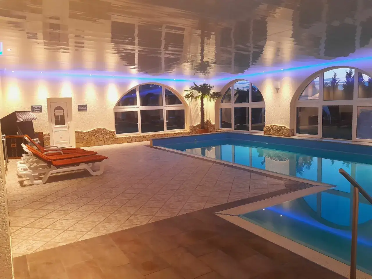 Entspannter Poolbereich im Carea Harz Hotel Allrode mit Liegen, Palmen und stimmungsvoller Beleuchtung.
