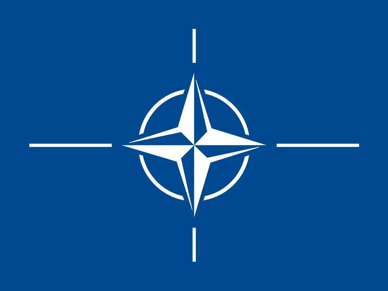 Flaga NATO: biała, czteroramienna gwiazda na tle niebieskiej tarczy, symbolizująca pokój i bezpieczeństwo.