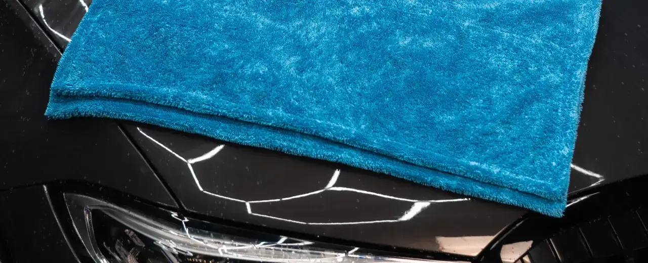 En blå mikrofiberduk vilar på den glänsande svarta motorhuven på en bil, redo för en Autoglym-finish.