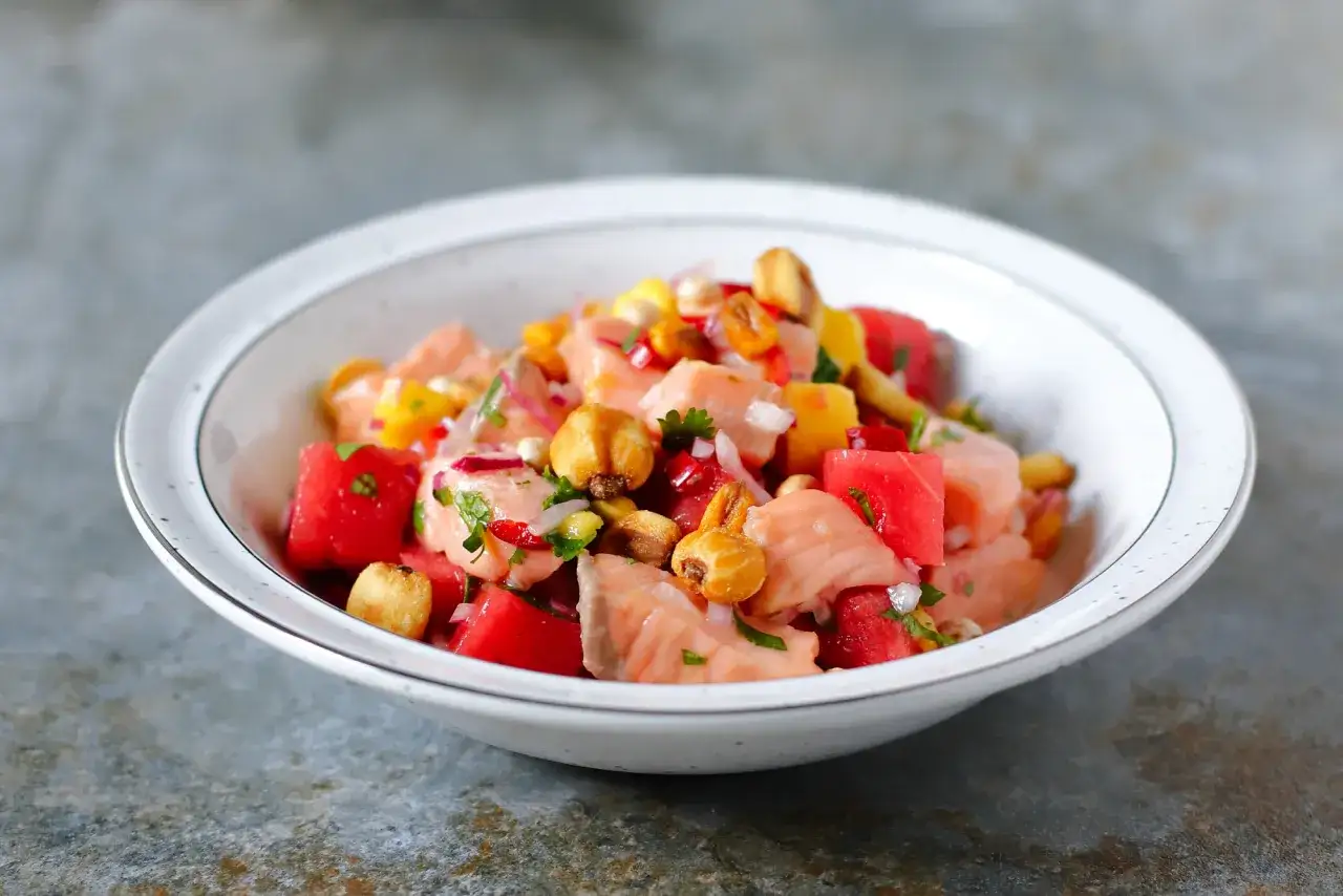 Kolorowe ceviche z łososia z kawałkami arbuza, kukurydzy i papryczki chili, podane w białej misce.
