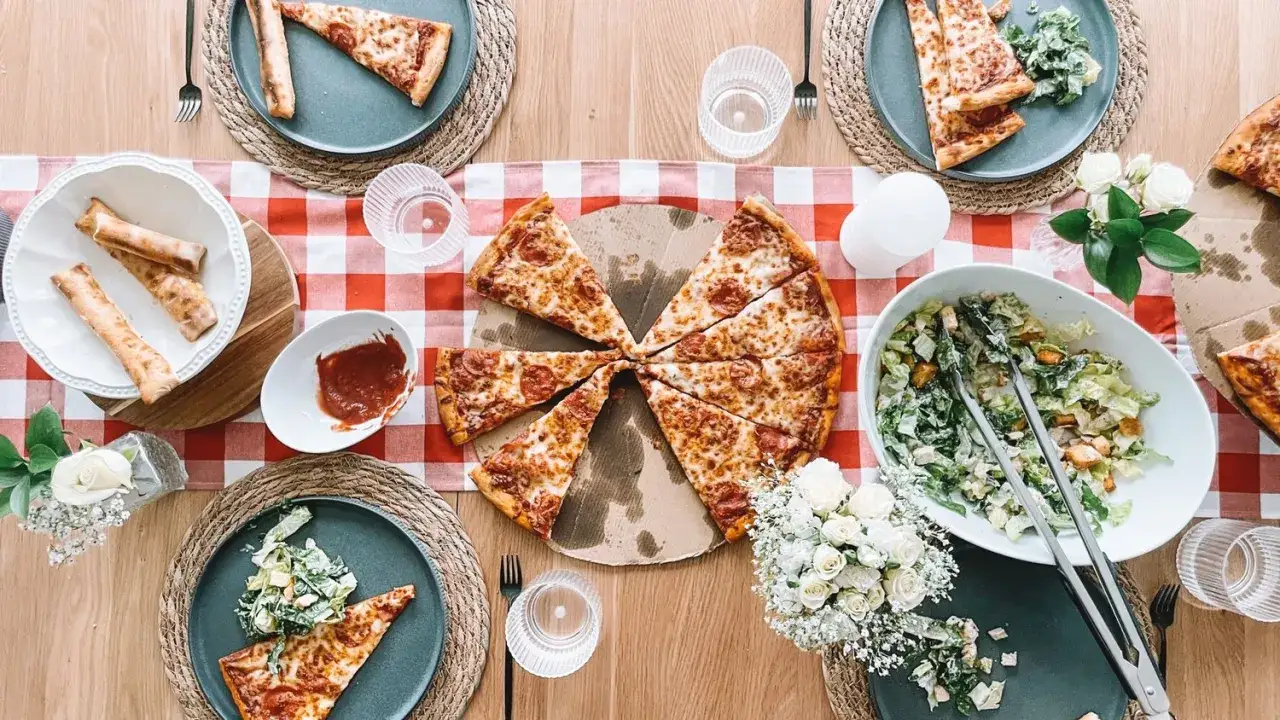 Idealny **dzień pizzy** z przyjaciółmi. Na stole pepperoni pizza, sałatka Cezar, paluszki serowe i sos.