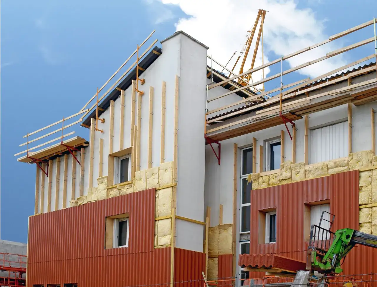 Chantier de construction : pose de l'isolant et des bardages pour une isolation par l'ext&eacute;rieur. Grue et &eacute;chafaudages visibles.