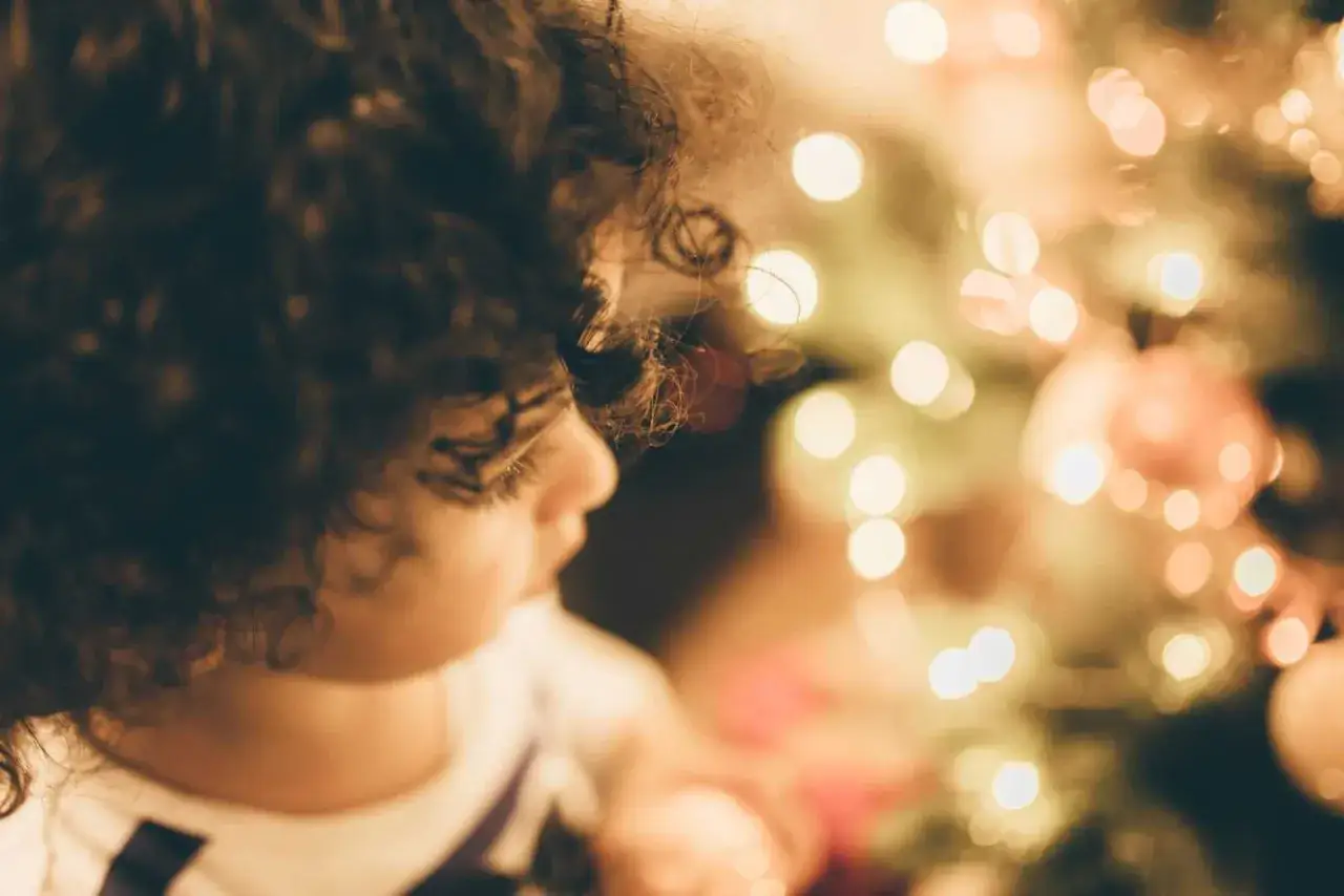 Ni&ntilde;o con rizos oscuros mira con asombro las luces de un &aacute;rbol de Navidad, reviviendo las leyendas de Navidad.
